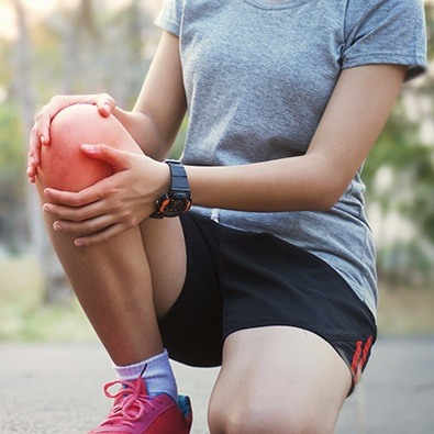 Woman on a run with patellofemoral syndrome holding knee in pain