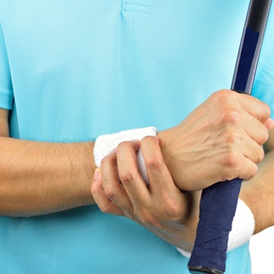 man with tennis racket holding sore wrist 