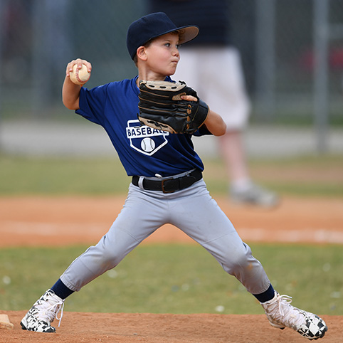 Little boy playing baseball after little league elbow treatment