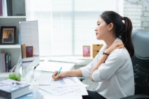 woman experiencing neck pain while working 